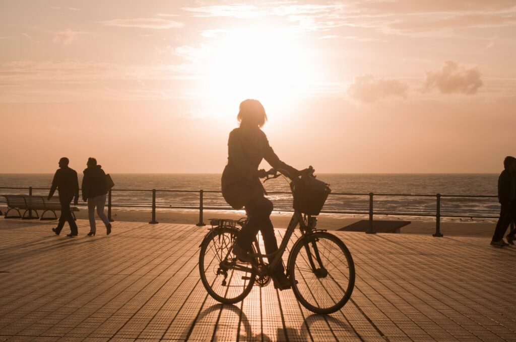 Femme à vélo dans les rayons du soleil couchant sur la digue à Ostende